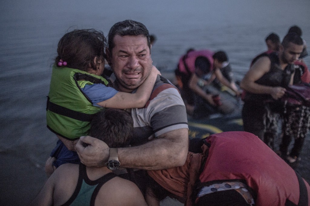 A Syrian refugee from Deir Ezzor, holding his son and daughter, breaks out in tears of joy after arriving via a flimsy inflatable boat crammed with about 15 men, women and children on the shore of the island of Kos in Greece, Aug. 15, 2015. Photo: Daniel Etter/The New York Times