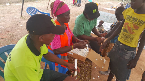 Ulkomaanavun työntekijät auttoivat kiinnittämään rannekkeita Pohjois-Ugandan vastaanottokeskuksessa. Rannekkeiden avulla varmistetaan, että jokainen pakolainen rokotetaan.