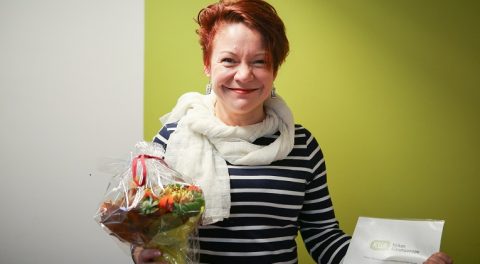 Nainen katsoo kamenraan kukkakimppu kädessä