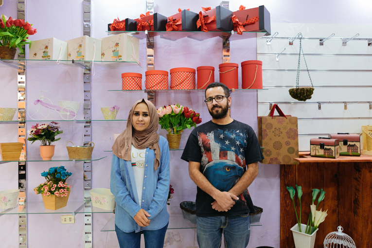 Asma'a and Hussam standing in front of the shelves with gift packages in their shop.