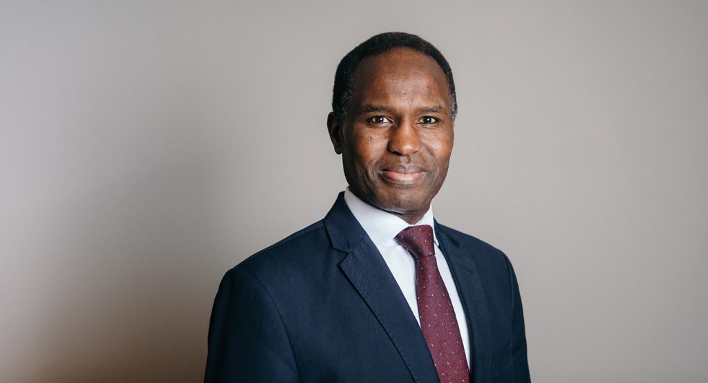 A smiling man in a suit jacket and tie poses for the camera