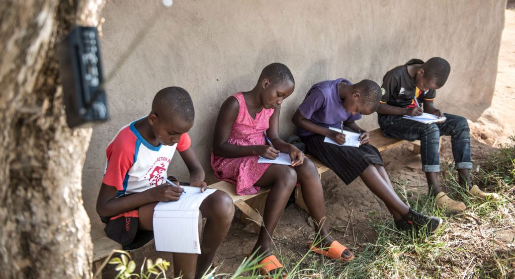 Neljä ugandalaista koululaista istuu penkillä keskittyneenä kirjoittamaan vihkoihinsa