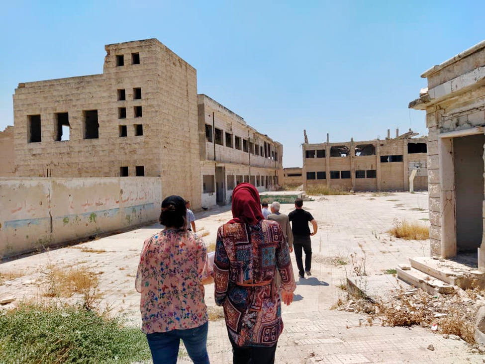 People walking on scoold yard. School buildings in the background are damaged by the war.