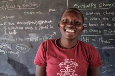 Viola smiles happily in front of a blackboard full of text.