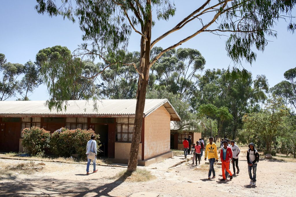 A building, trees and a couple of young people walking in the sun.