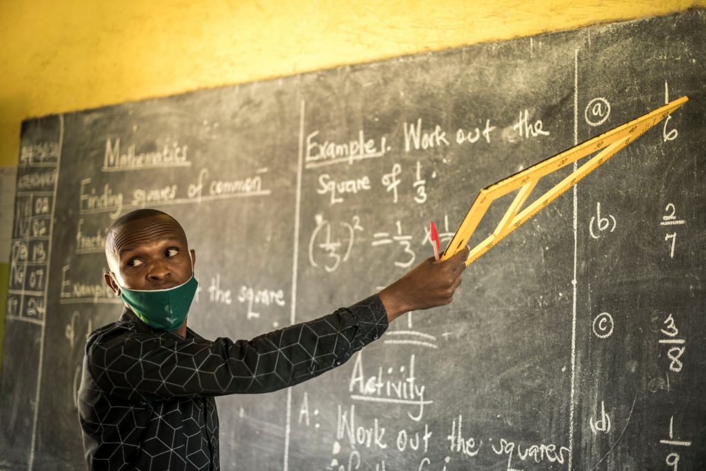 Felix Tumwesigye points to something on the blackboard and looks back at his students.