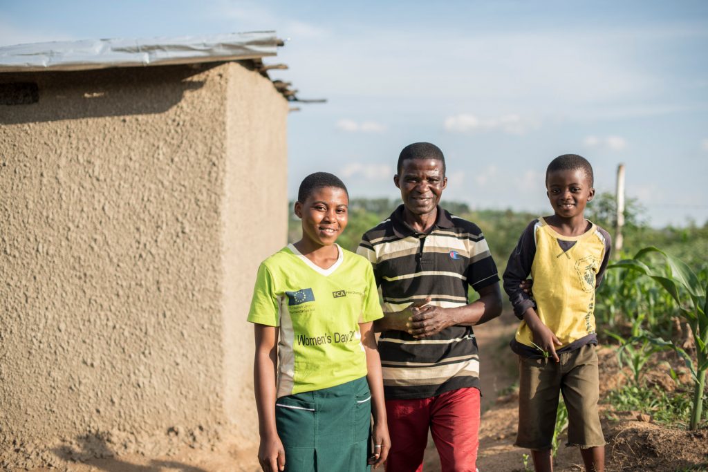 Joyce, her father and brother smiling outdoors in the sun.