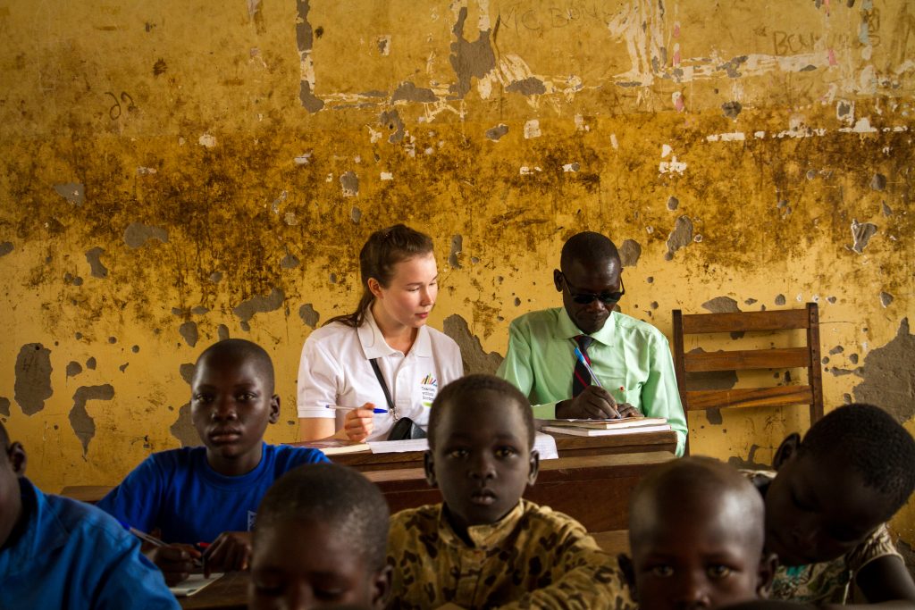 A Teachers without Borders volunteer with a local teacher talking at the back of a classroom.