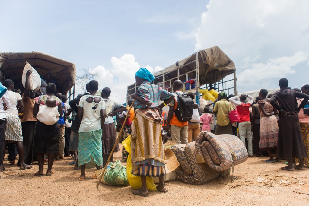 People with baggage queuing to get supplies from vans.