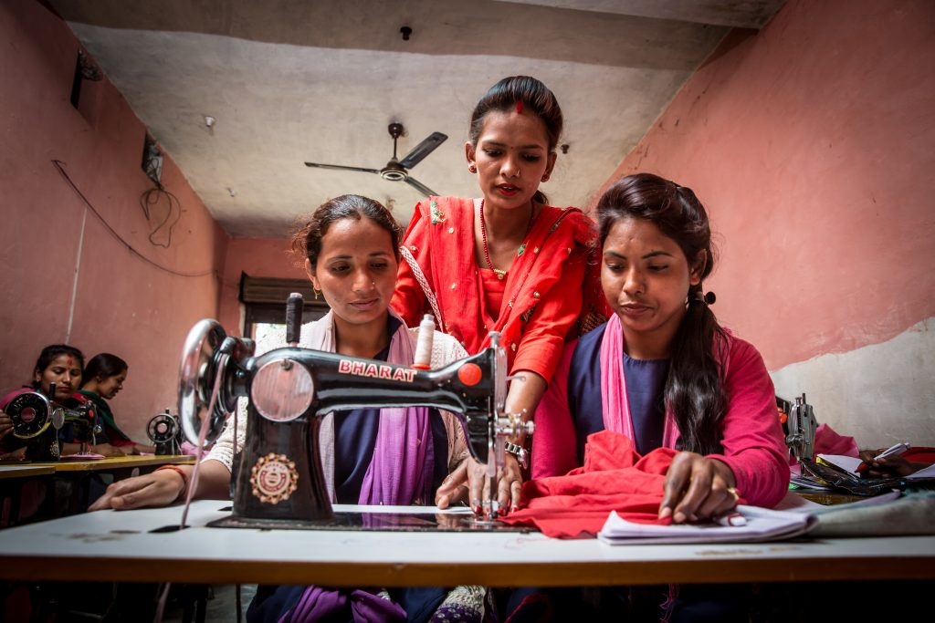 Three women gathered around sewing machine.