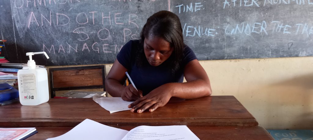 A woman sitting at a desk in front of a blackboard.