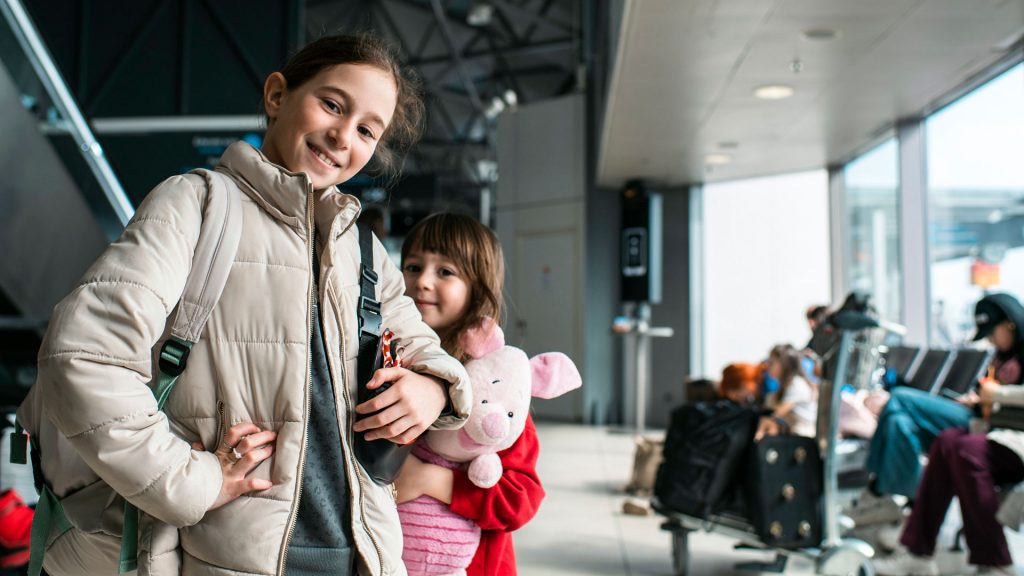 Two girls, one of them holding a Piglet doll. More people sitting in the background.