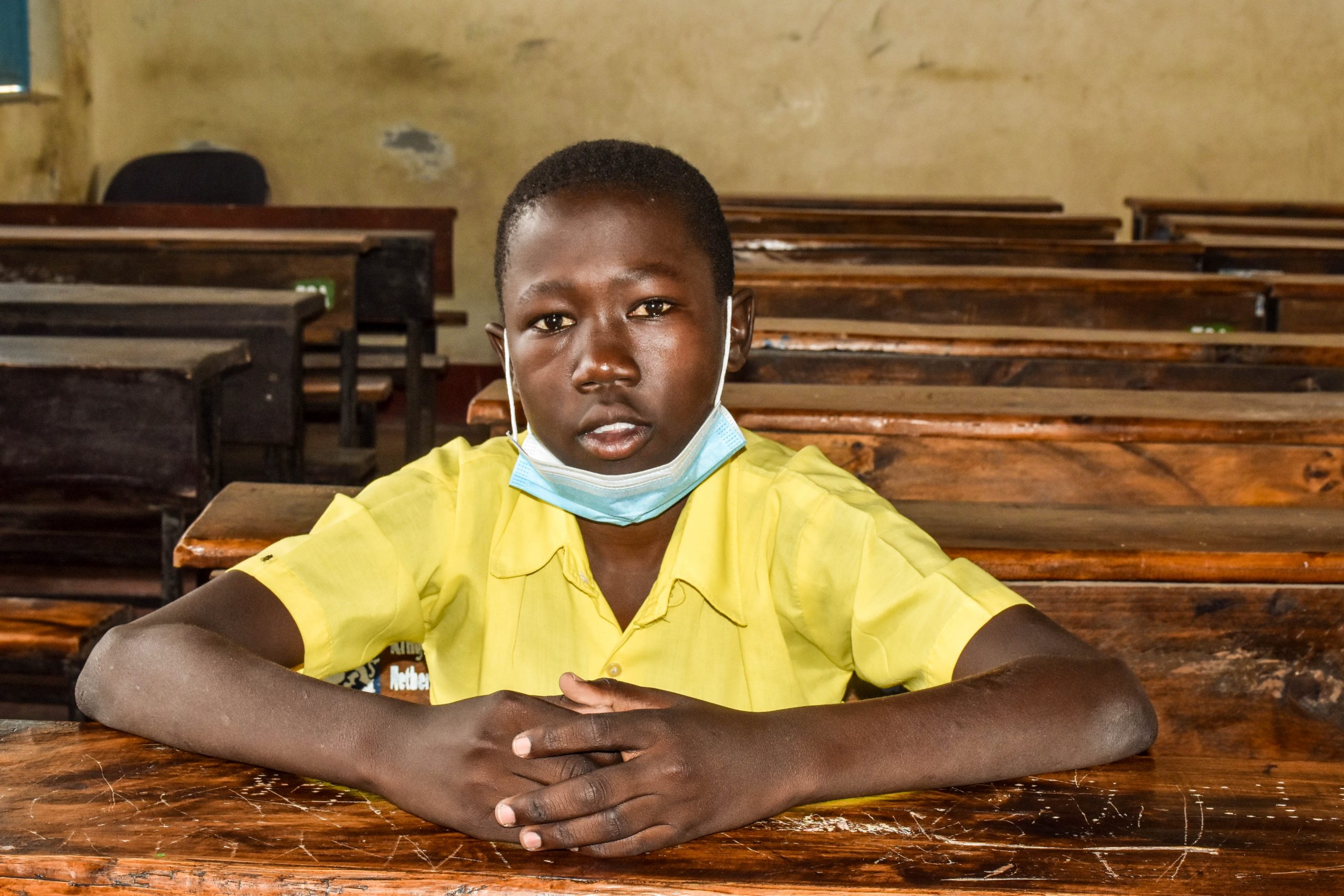 A young Kenyan boy sits at a desk in a classroom.