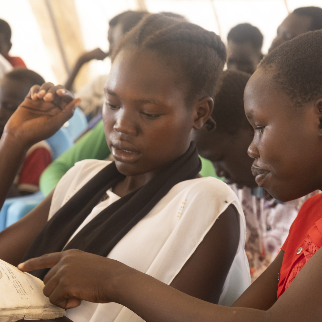 Two schoolgirls confer in a full classroom in New Fangak