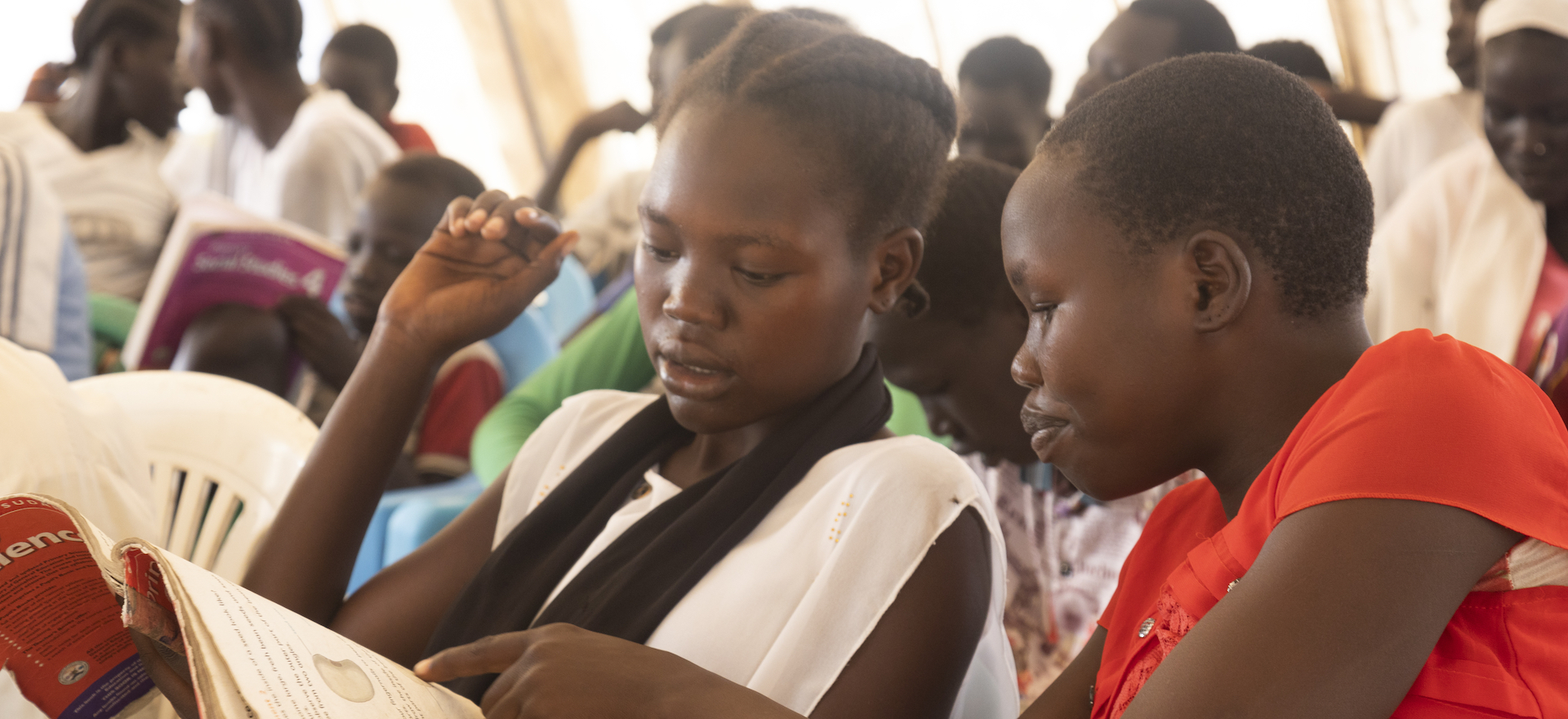 Two schoolgirls confer in a full classroom in New Fangak