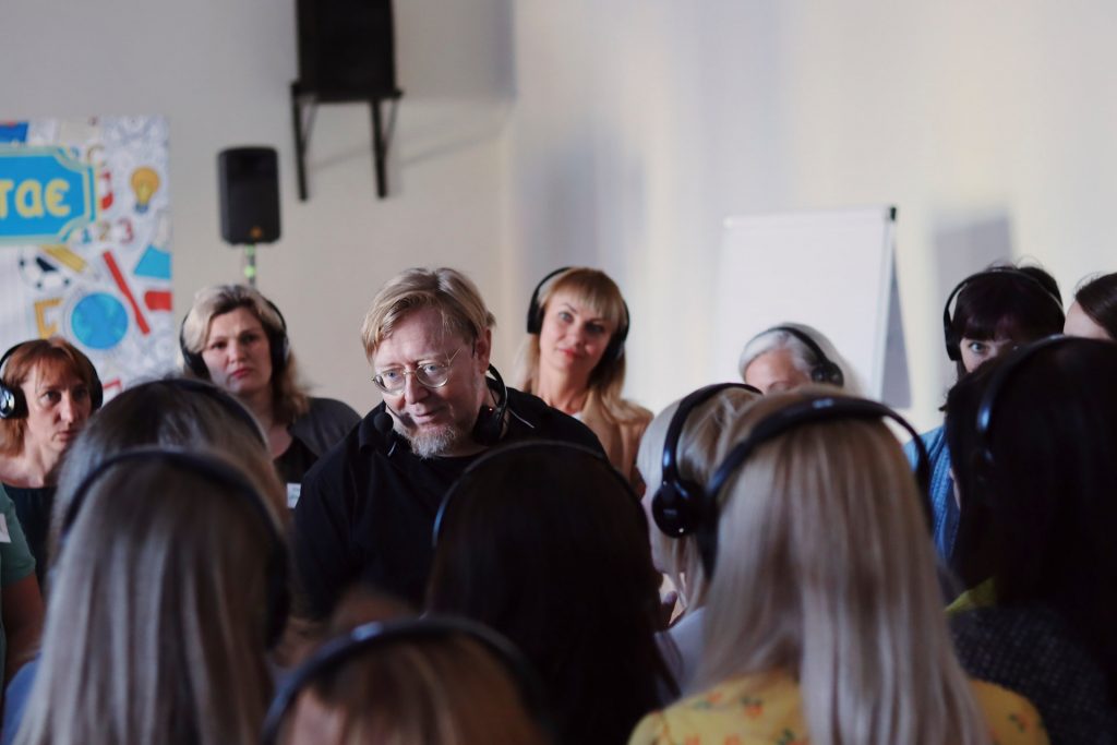 A man stands in the middle of a circle of women, who are wearing headphones
