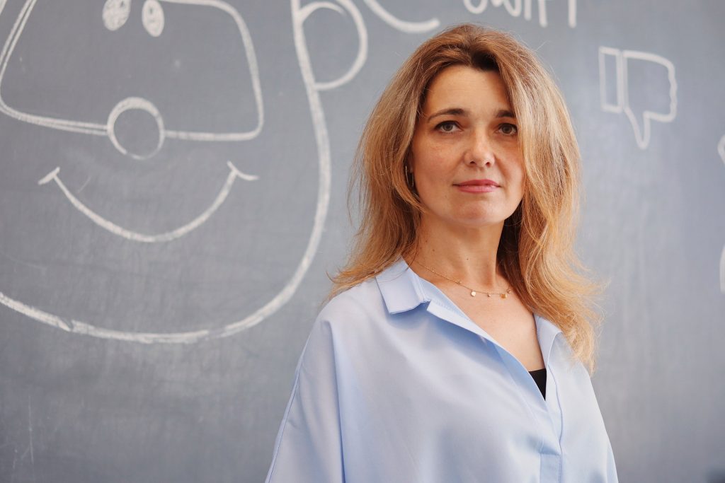 A woman stands in front a blackboard looking to camera