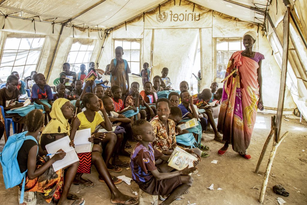 A female teacher stands smiling in front of a class in a tent