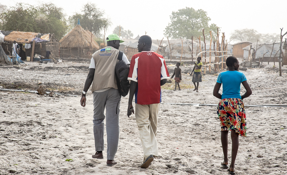 Two men and a girl walk through a village, partially destroyed by flooding.