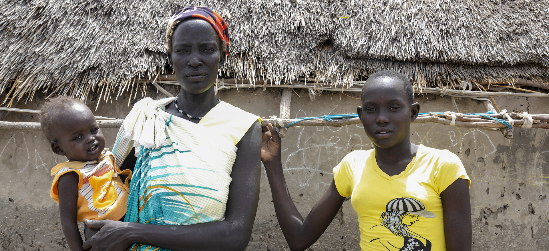 A woman holds a baby in front of a hut in New Fangak, South Sudan
