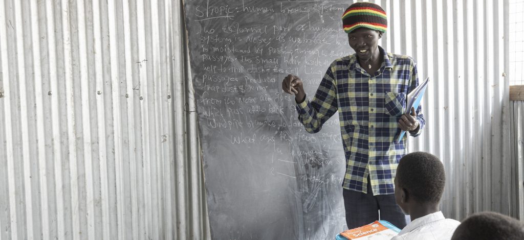 A man stands in front of a blackboard, teaching a class of pupils