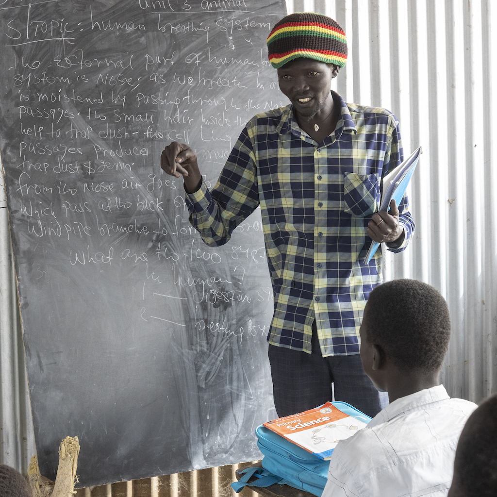 A man stands in front of a blackboard, teaching a class of pupils
