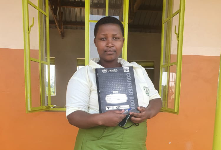 A woman standing in front of a window holding a notebook. 