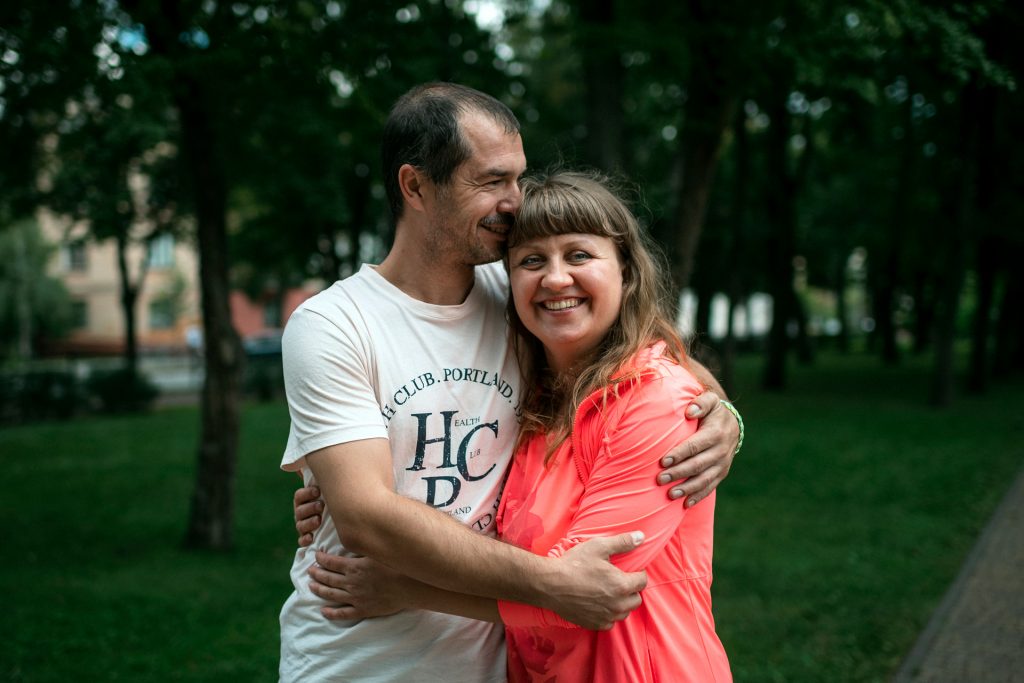 A man and a woman are hugging each other. The woman is smiling. The couple stands in a park with trees behind them. Photo: Antti Yrjönen / FCA