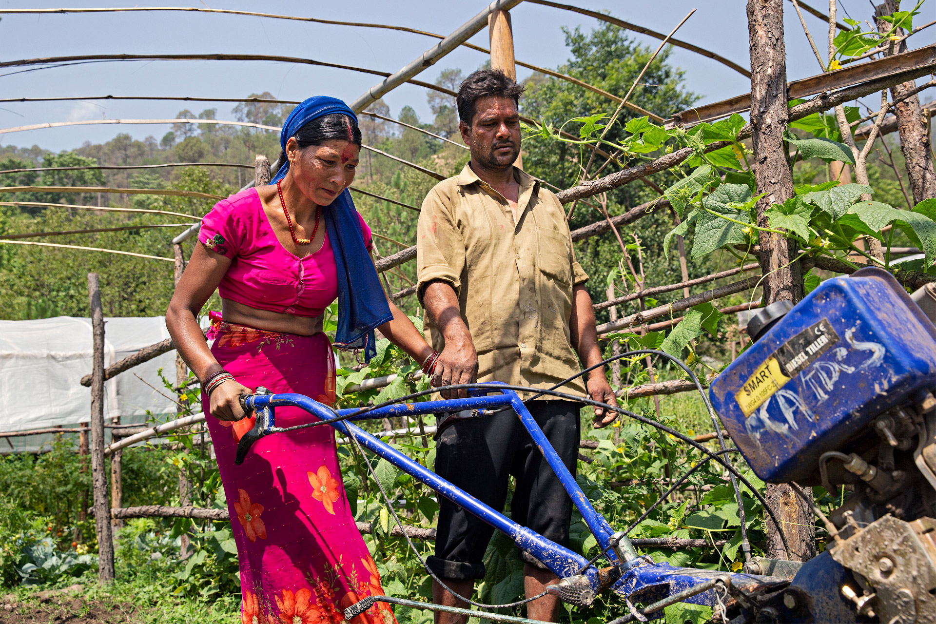 A woman is holding a hand tracktor. A man is walking next to the woman.