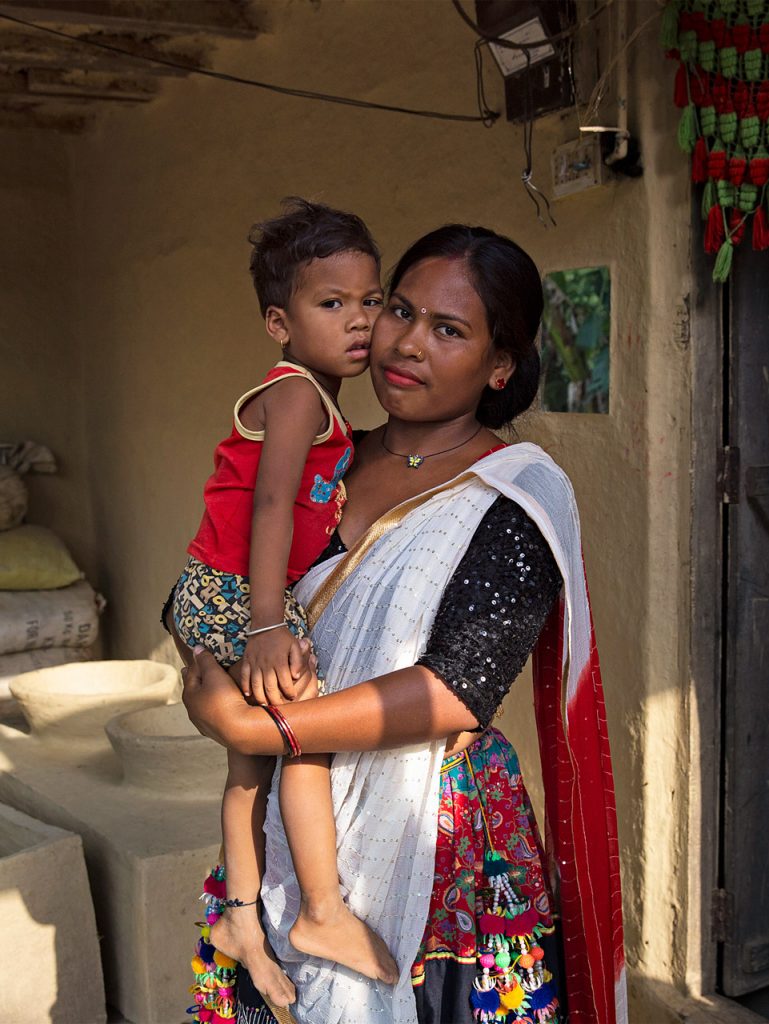 A Nepalese woman is standing in a room holding her young child in her arms.