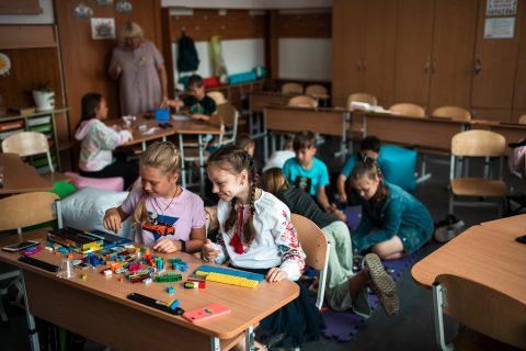 Kaksi tyttöä istuu pulpetissaan rakentamassa legoilla Ukrainassa. Luokkahuoneessa on muitakin lapsia. Kuva: Antti Yrjönen / KUA