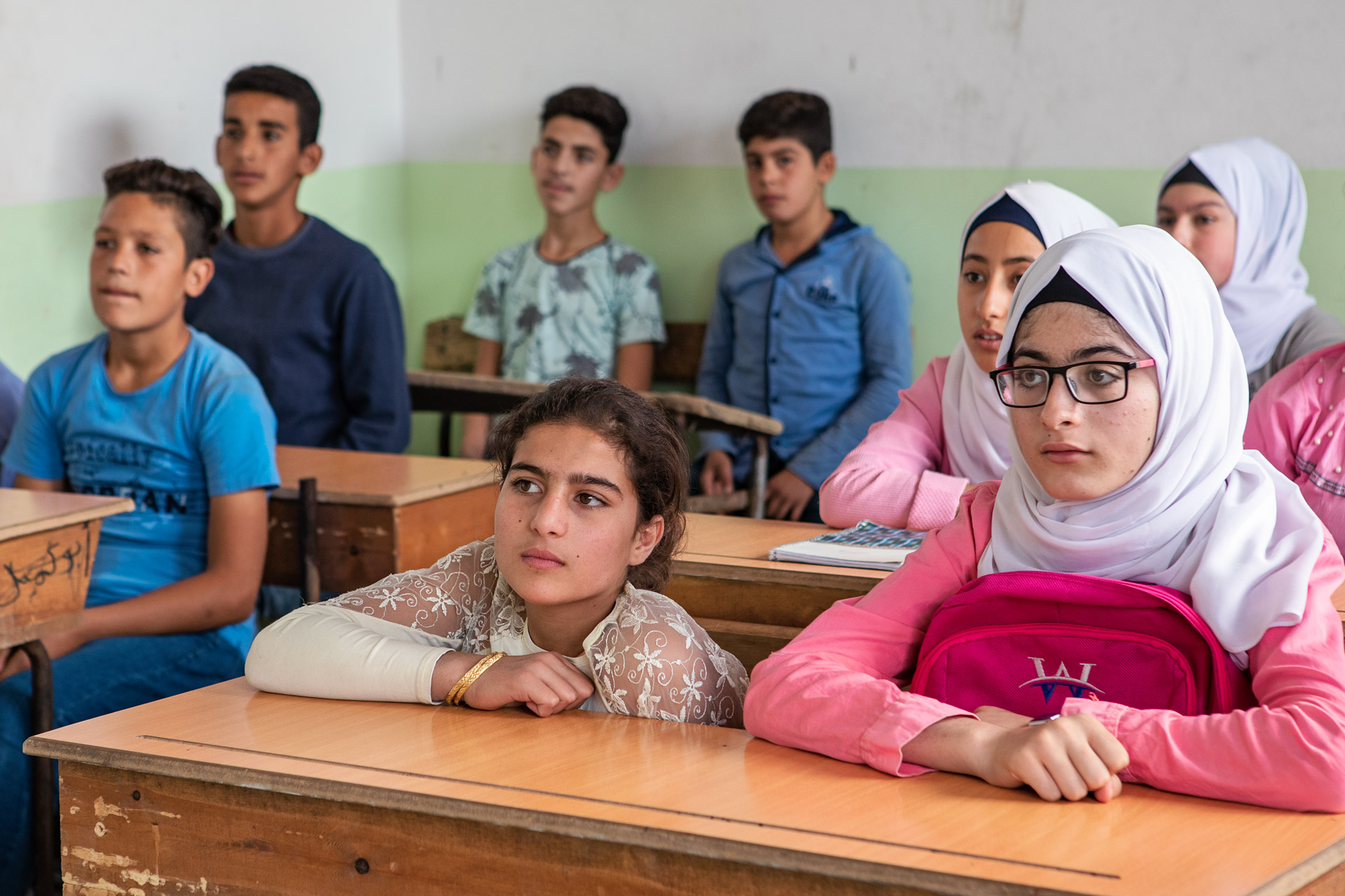 Girls and boys sit behind their desks in a class room and listen to their teacher.