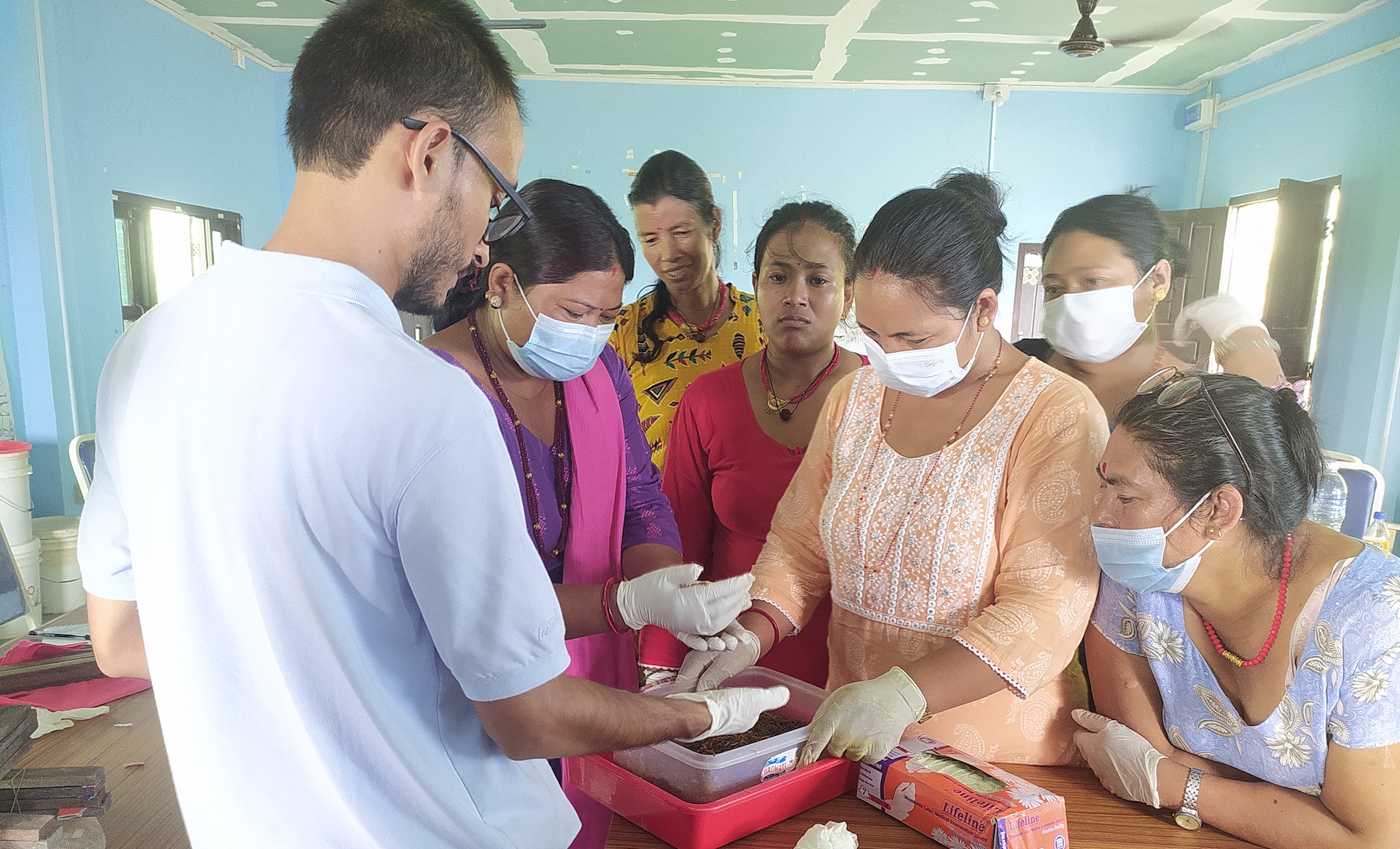 Women gather round a man holding larvae at a demonstration of how black soldier fly larvae can be bred for animal feed in Nepal