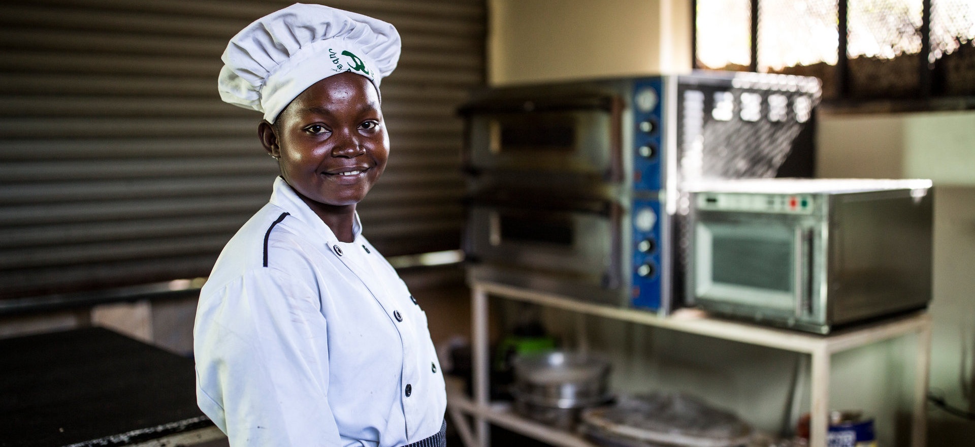 A woman in a chef's hat stands in a kitchen.