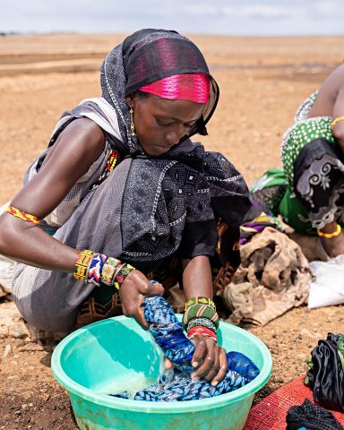 A Kenyan woman sits on the ground outside and washes clothes with her hands.