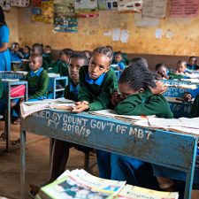 lapset istuvat koululuokassa pulpeteissaan Keniassa. Pöydillä on kirjoja ja vihkoja.