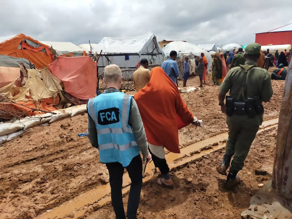 People, photograpghed from behind, walking in a refugee camp in Somalia. There are tents and more people behind. 