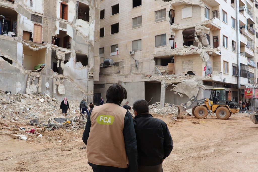 Kaksi miestä seisoo Syyriassa katsomassa sortuneita rakennuksia.