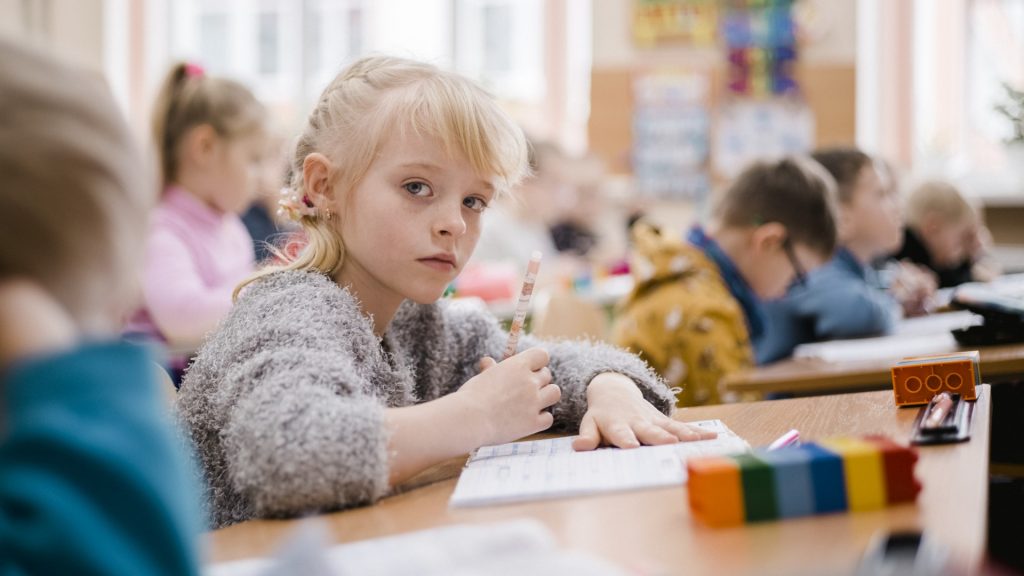 A schoolgirl looks up from her work in a busy classroom