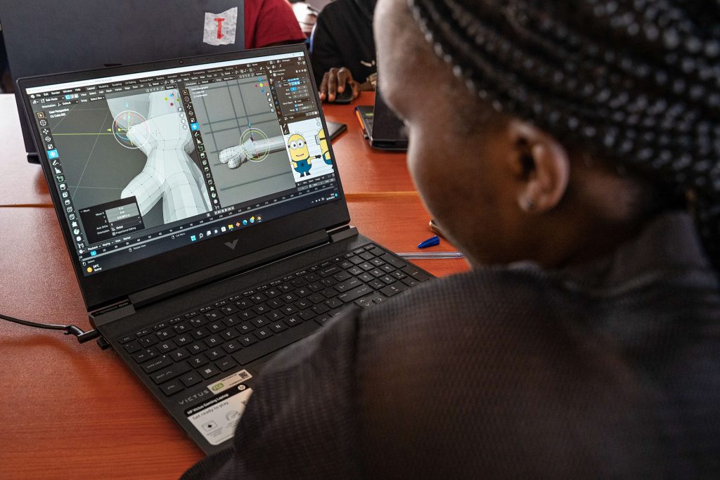 A woman sits at a laptop. On the screen is a 3D animation model. 