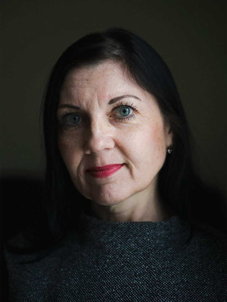 A woman looks at the camera in front of a dark background