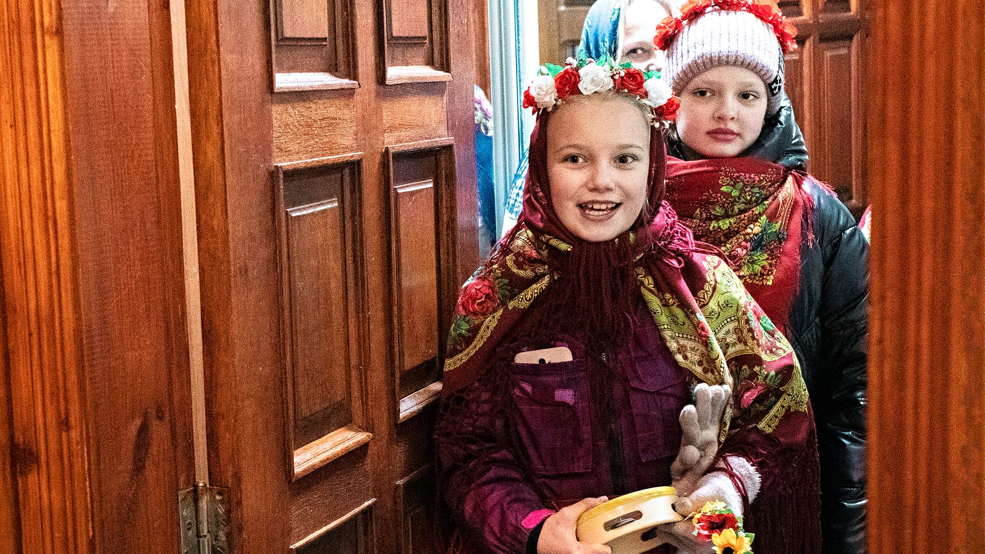 Two girls in Ukrainian national dress stand in a doorway singing.