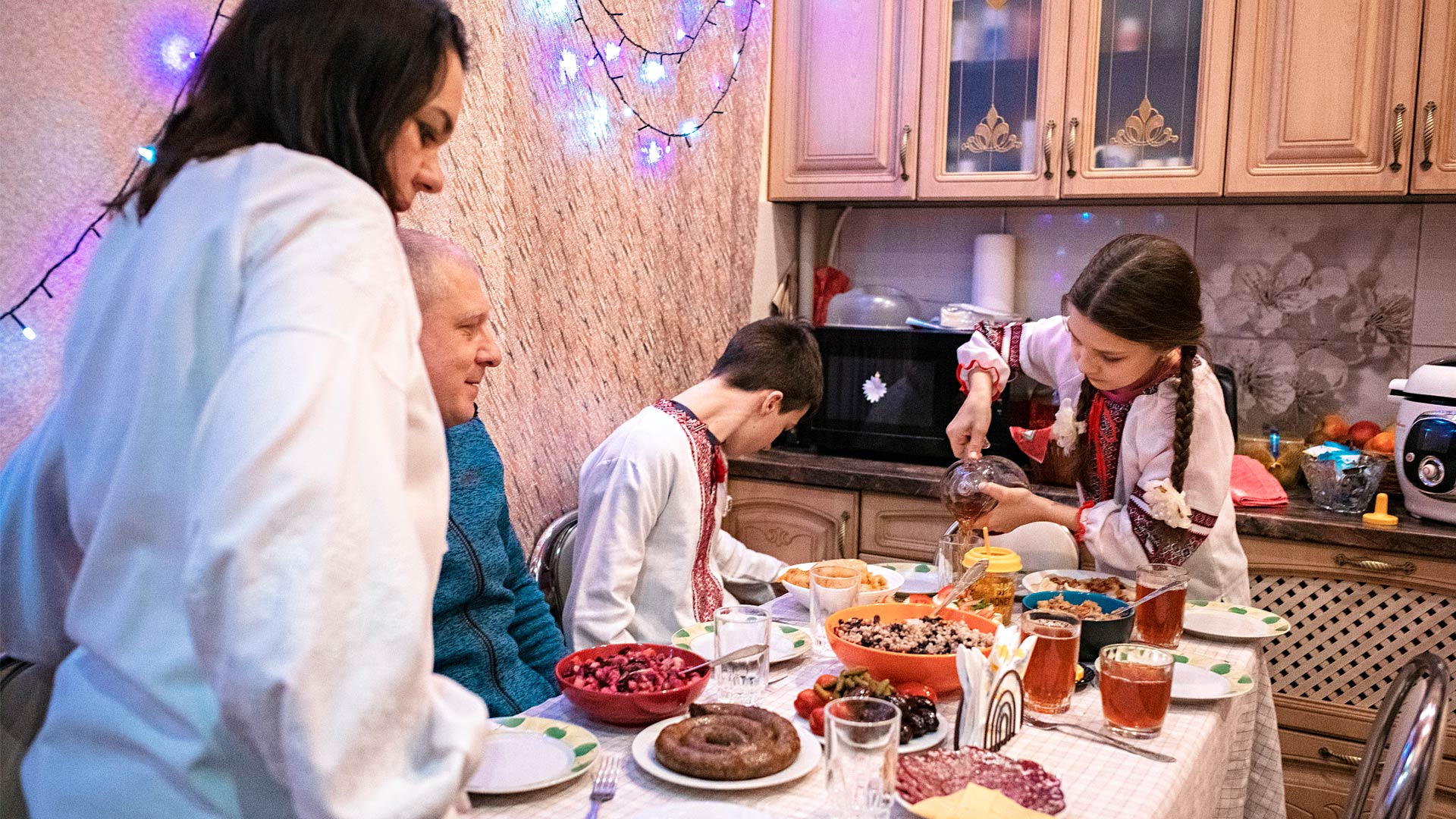 A family gather around a table full of food. A girl pours a drink.