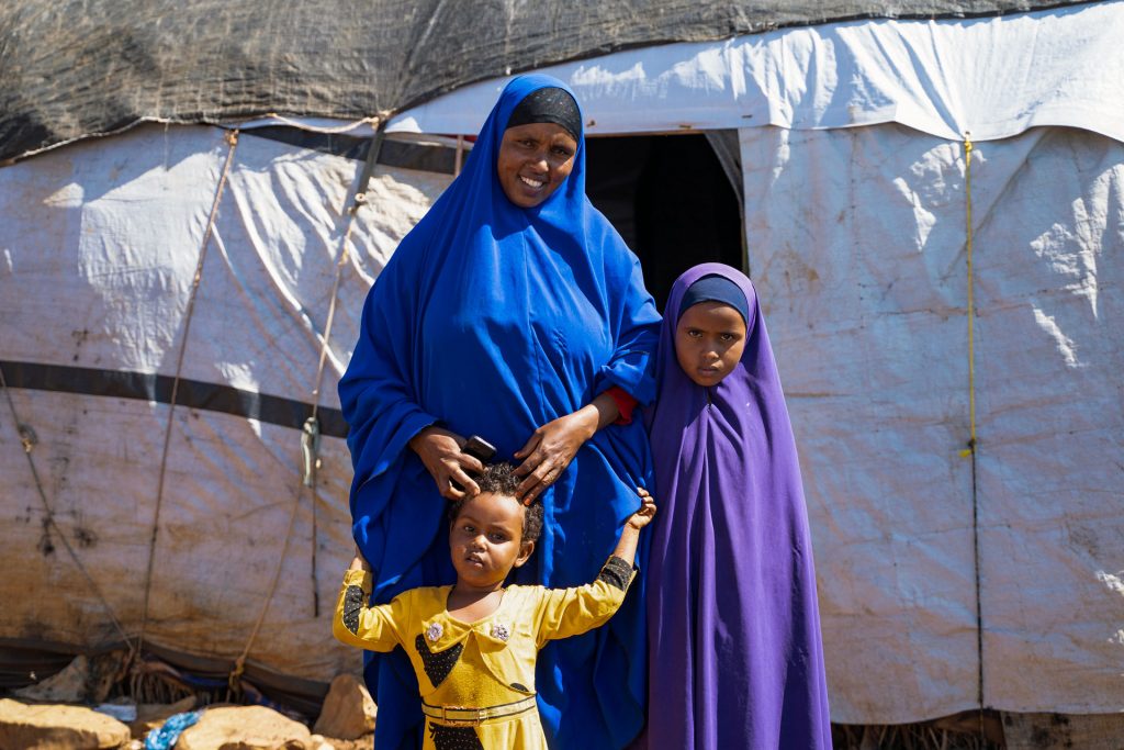 Somalialainen nainen ja kaksi lasta seisovat tilapäismajoitusteltan edessä.