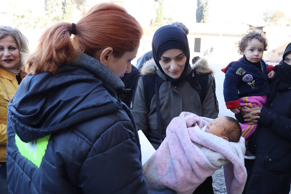 Two women holding a baby wrapped in a blanket.