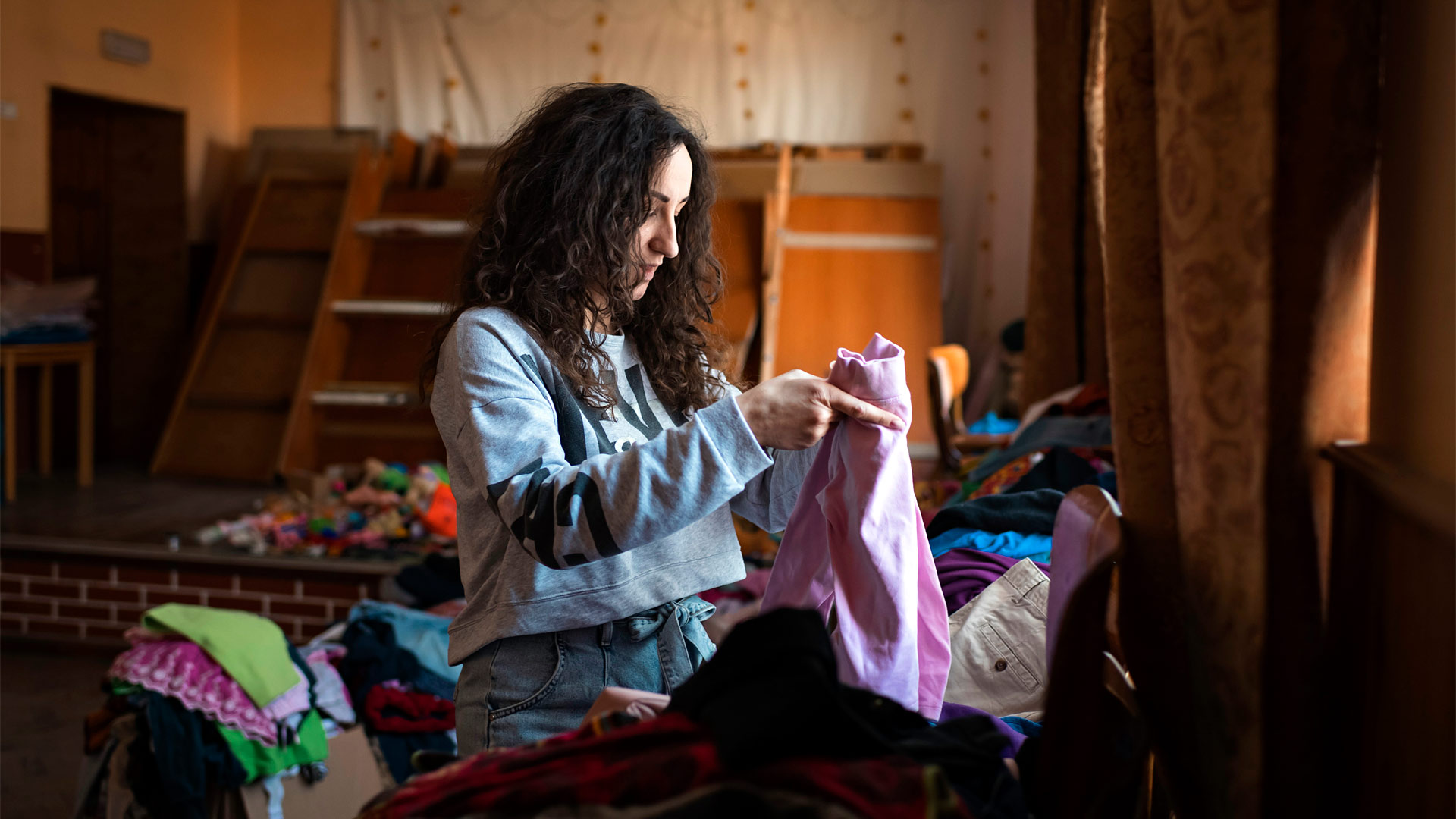 A woman folds clothes in an empty school assembly hall.