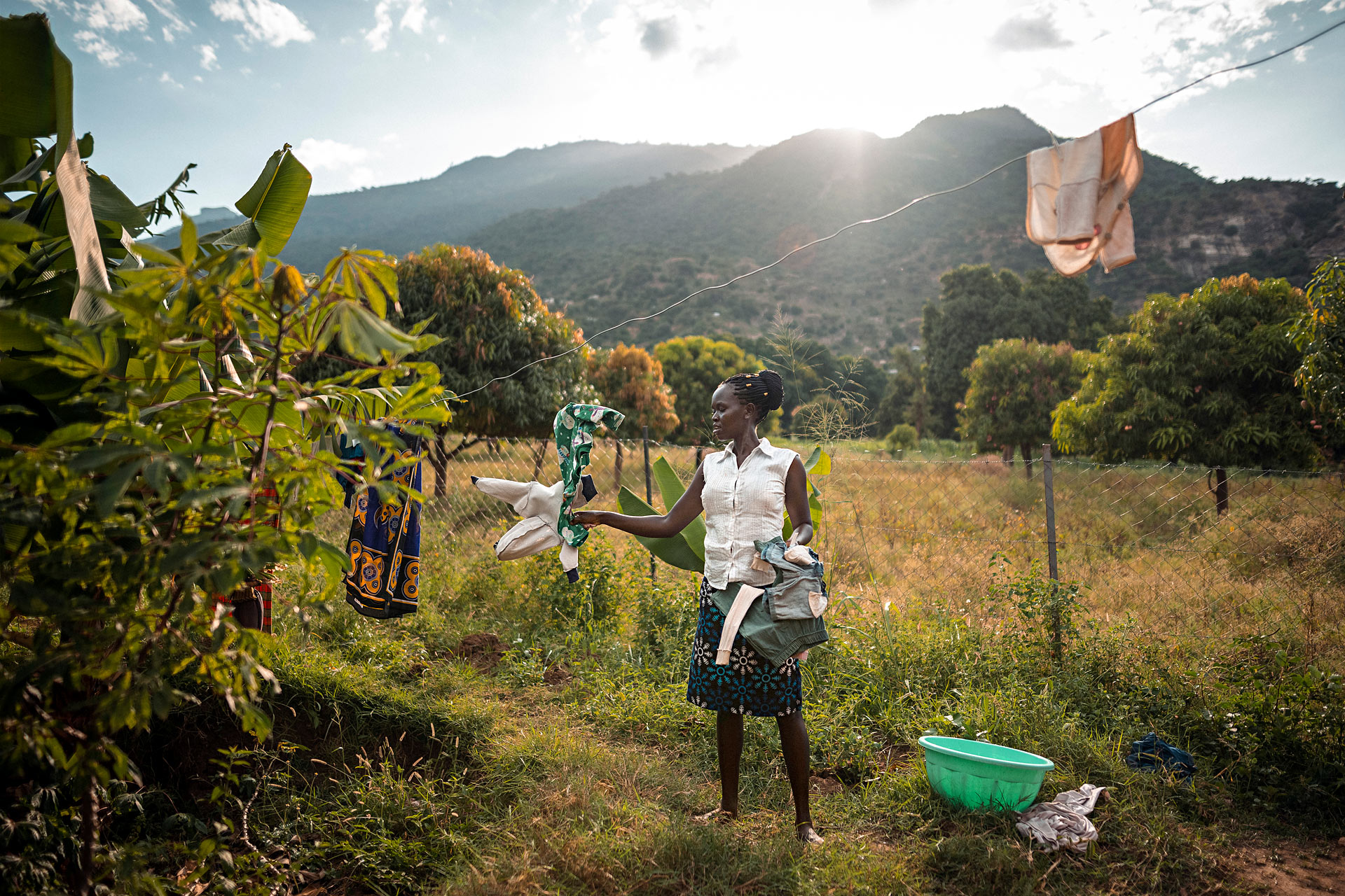 Nainen ripustaa pyykkiä kuivumaan ulos Keniassa. Taustalla näkyy kukkula.