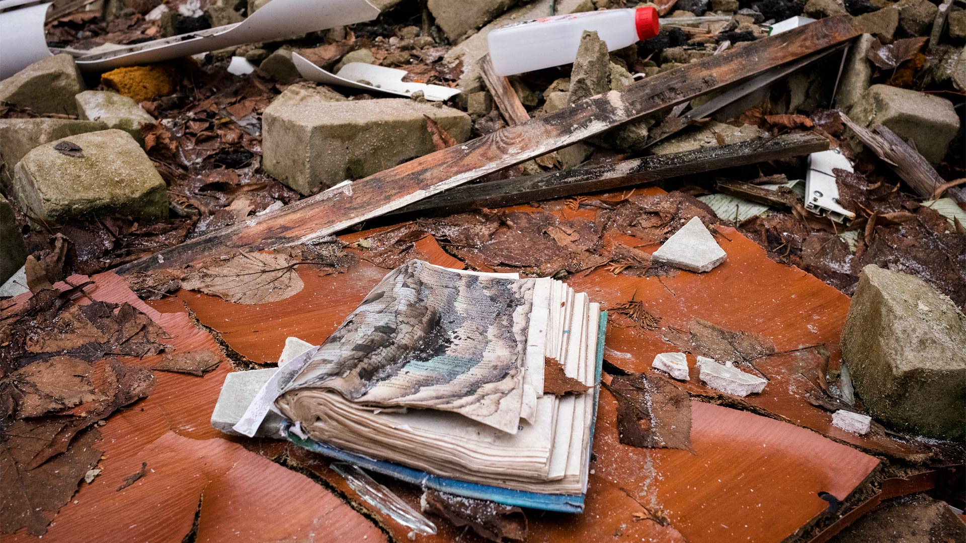 Rubble strewn on the ground. In the foreground is an open book with charred pages.