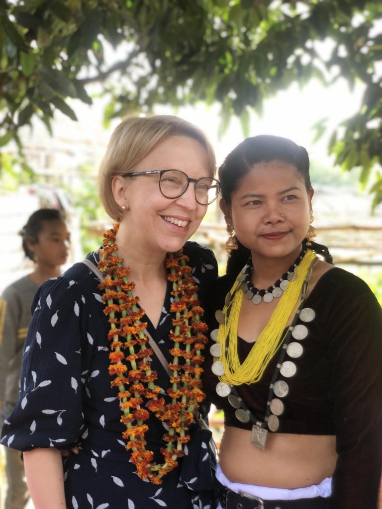 Two woman smile in a photo. They are both wearing large necklaces