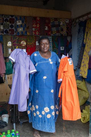 A woman standing and showing two school uniforms in different colours.